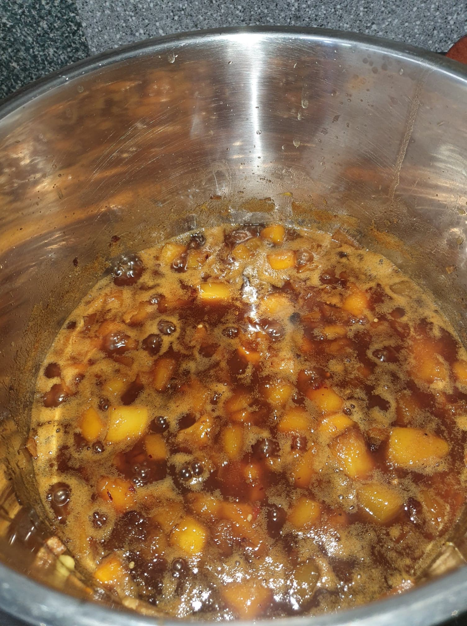 Finished chutney bubbling in the pot, with bright orange mango chunks in a glossy dark brown sauce